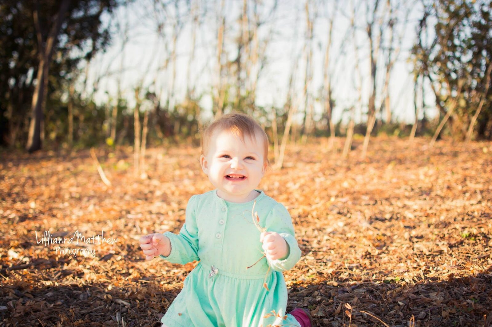 Baby girl laughing joyfully while sitting in autumn leaves, wearing a mint green dress