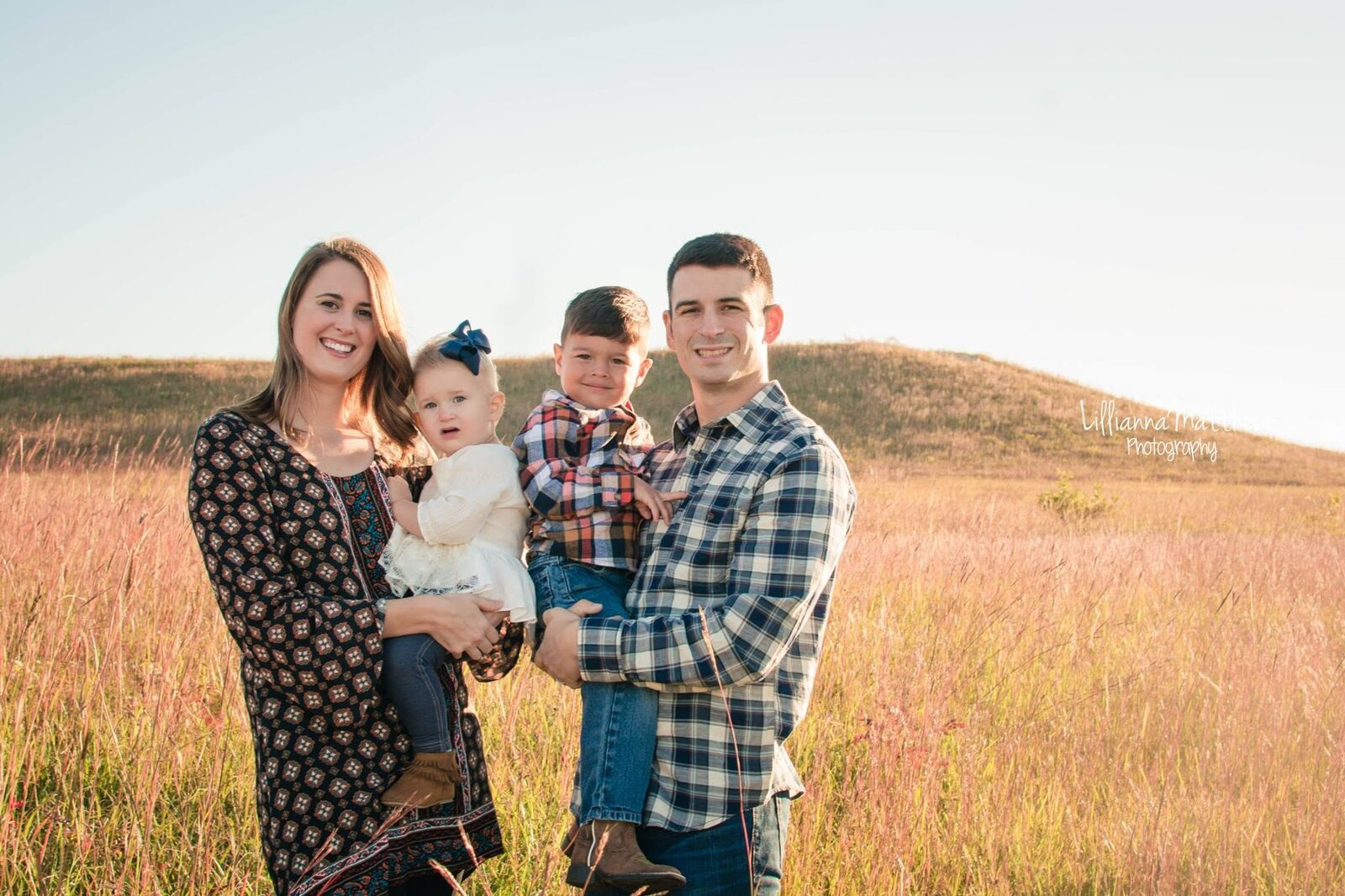 Family of four in coordinated plaid outfits standing together in a golden field