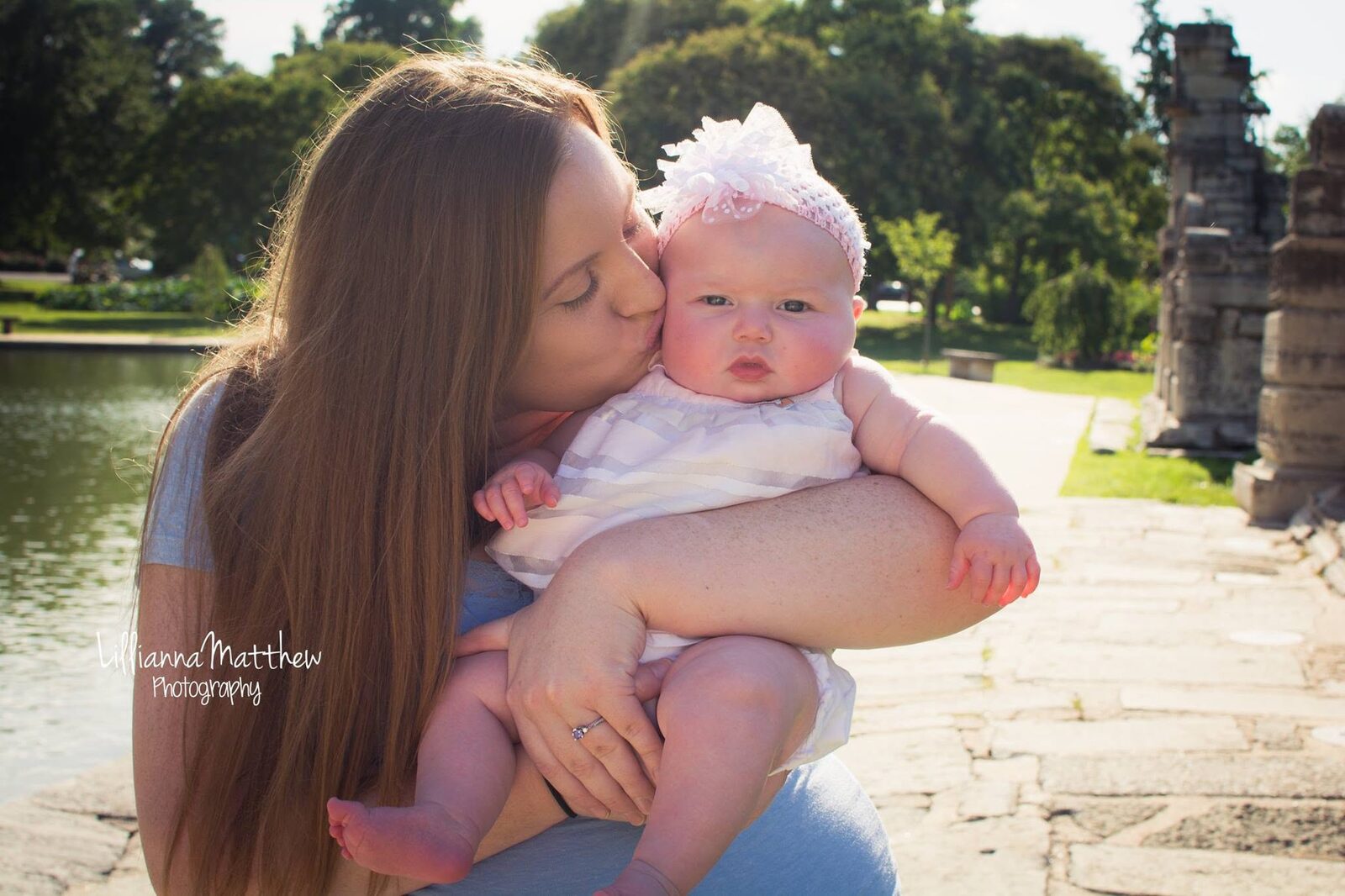Mother tenderly kissing her baby's head beside a park pond