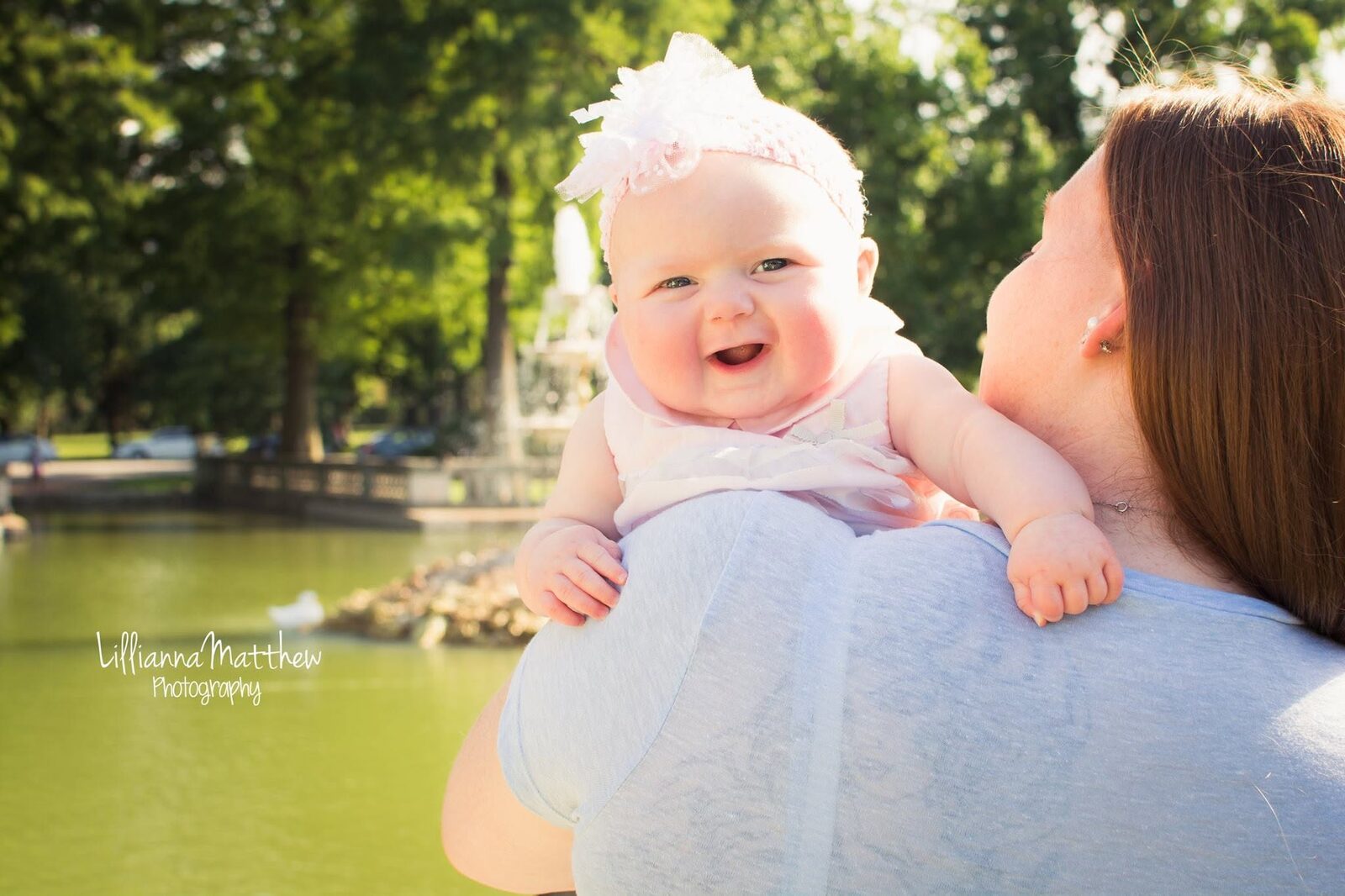 Baby laughing with a big genuine smile on mom's shoulder, bokeh fountain in the background