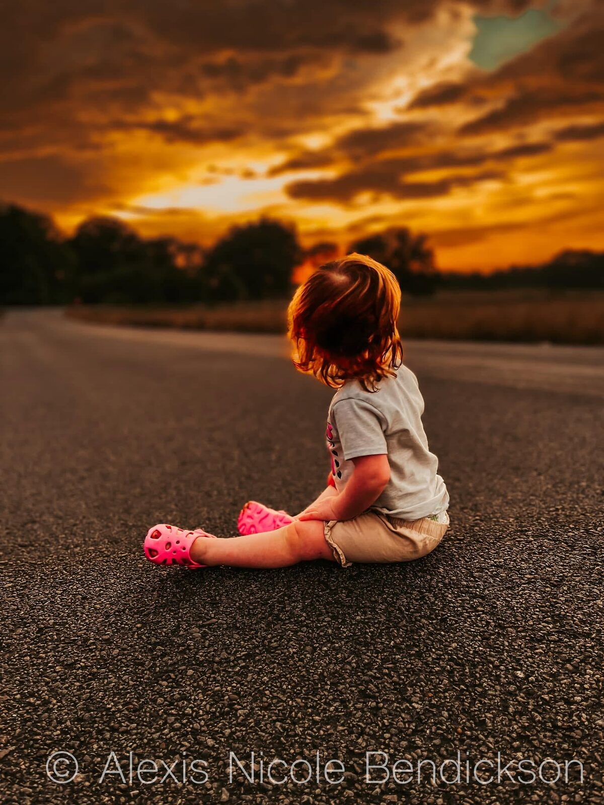 Toddler silhouetted against a dramatic orange and gold sunset sky with clouds