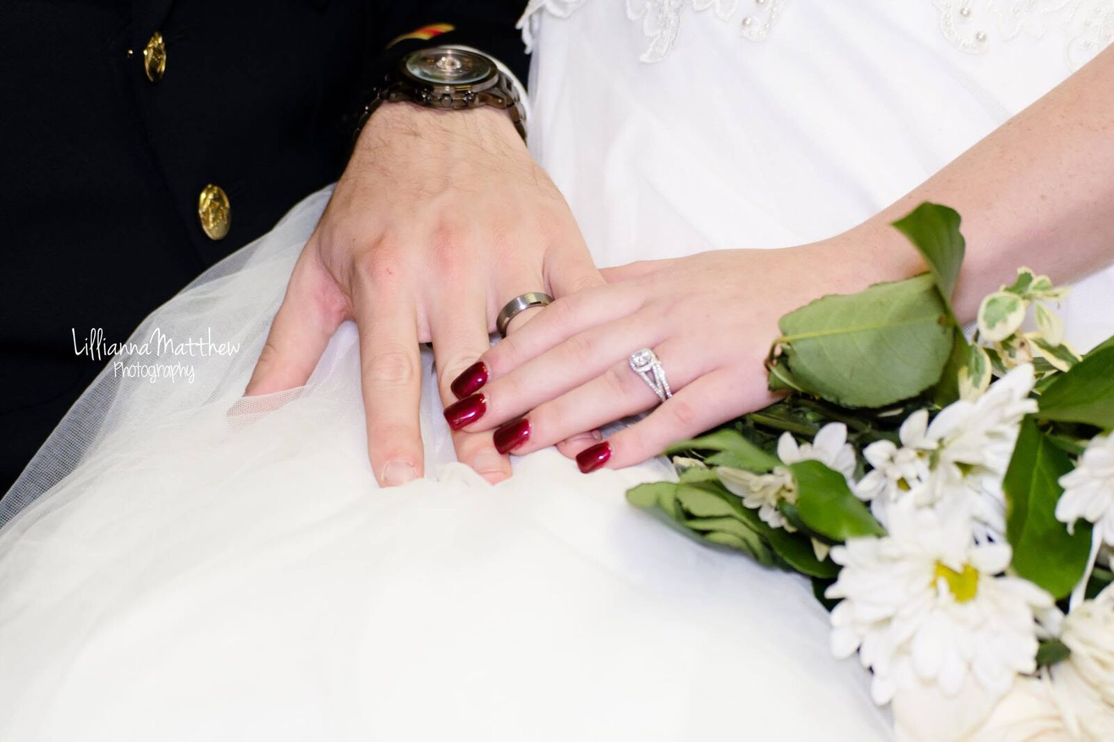 Close-up of bride and groom's hands showing wedding rings and a bouquet of white daisies