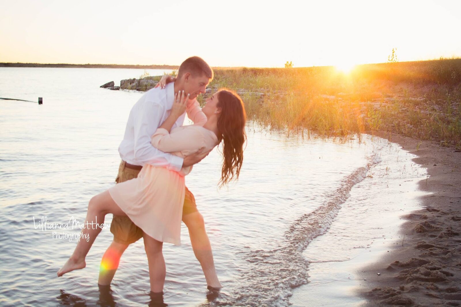 Couple embracing at sunset by the water with a romantic sun flare