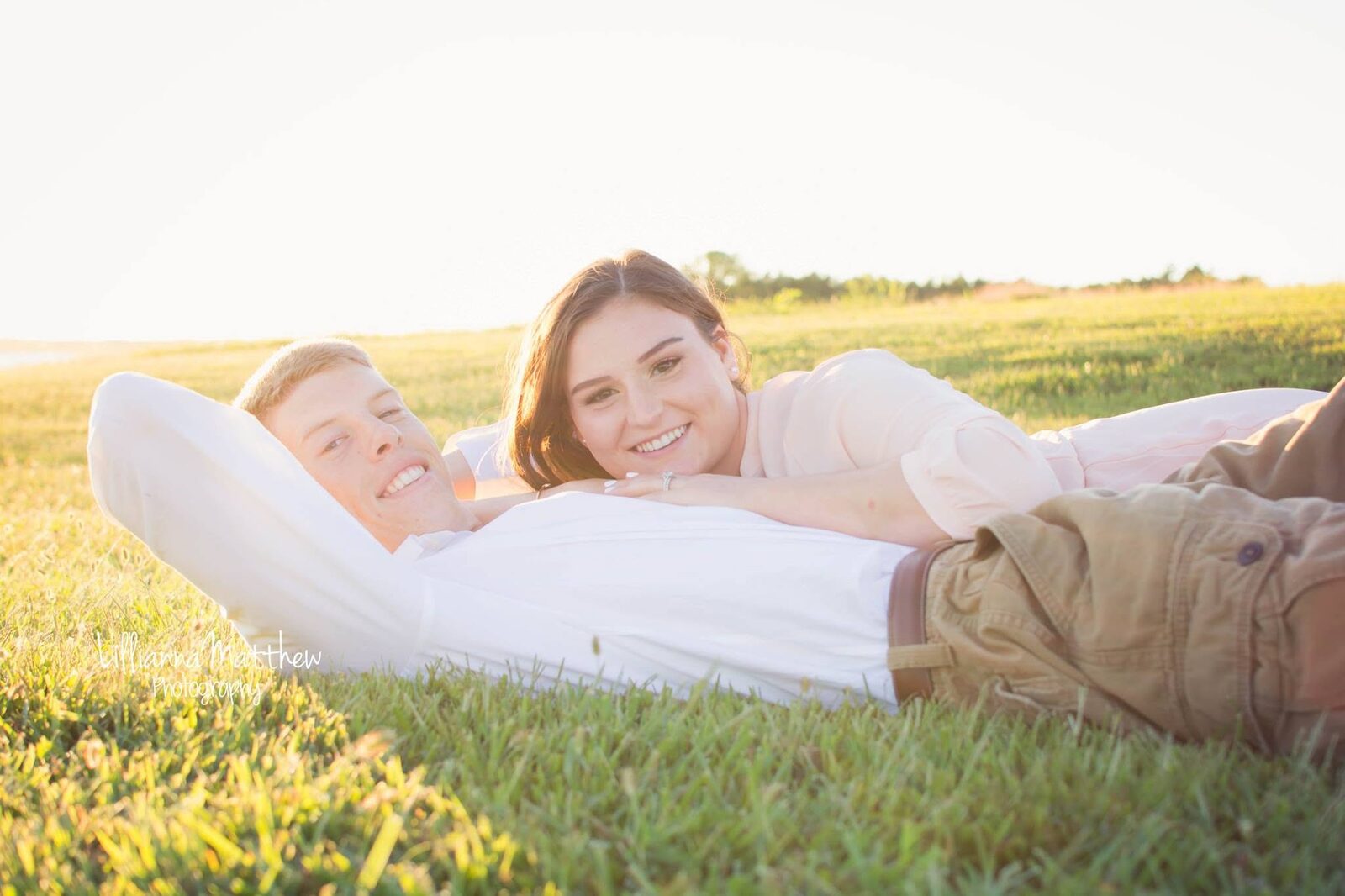 Couple lying in golden grass, both smiling candidly at the camera