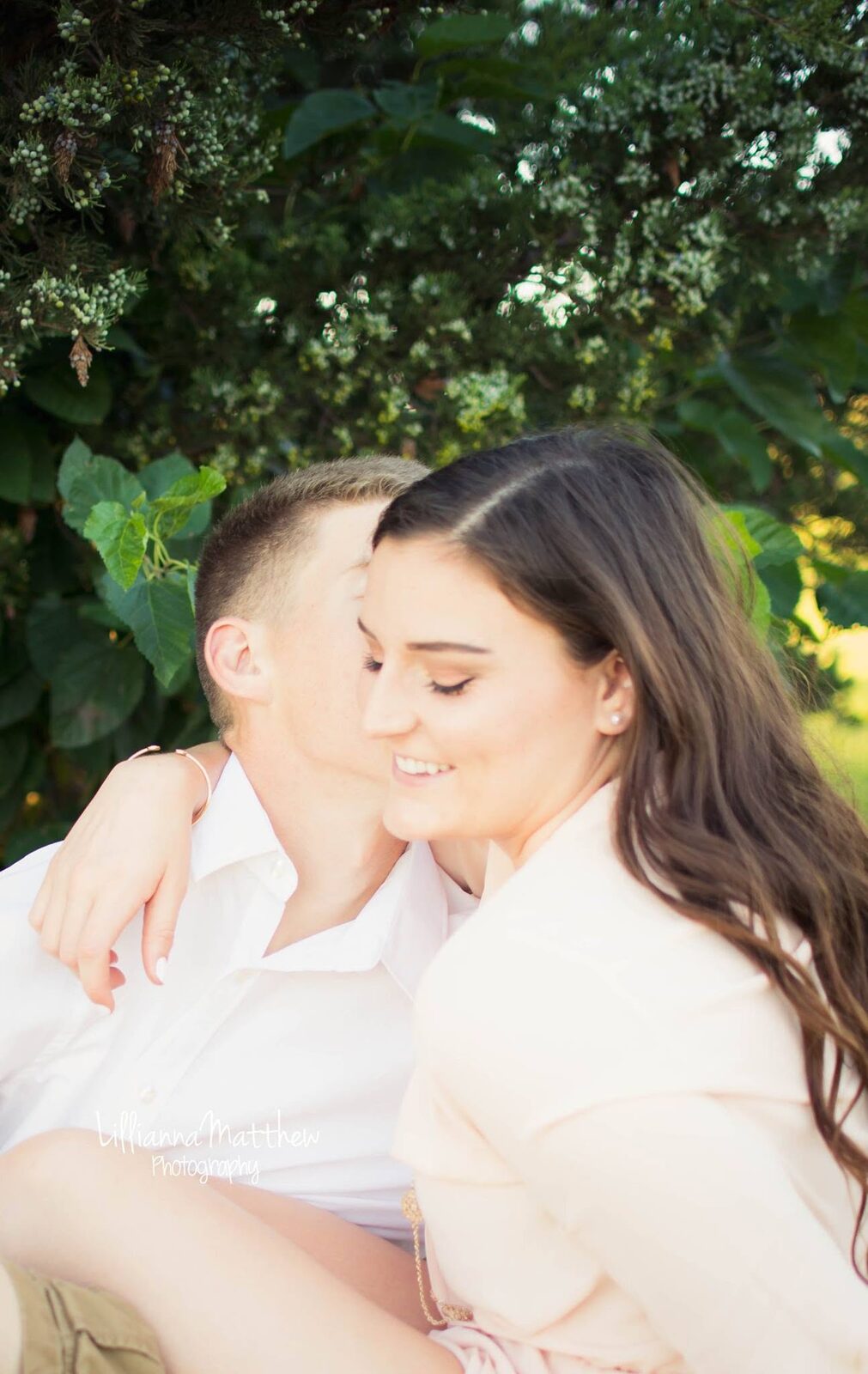 Intimate cheek-kiss embrace among green foliage