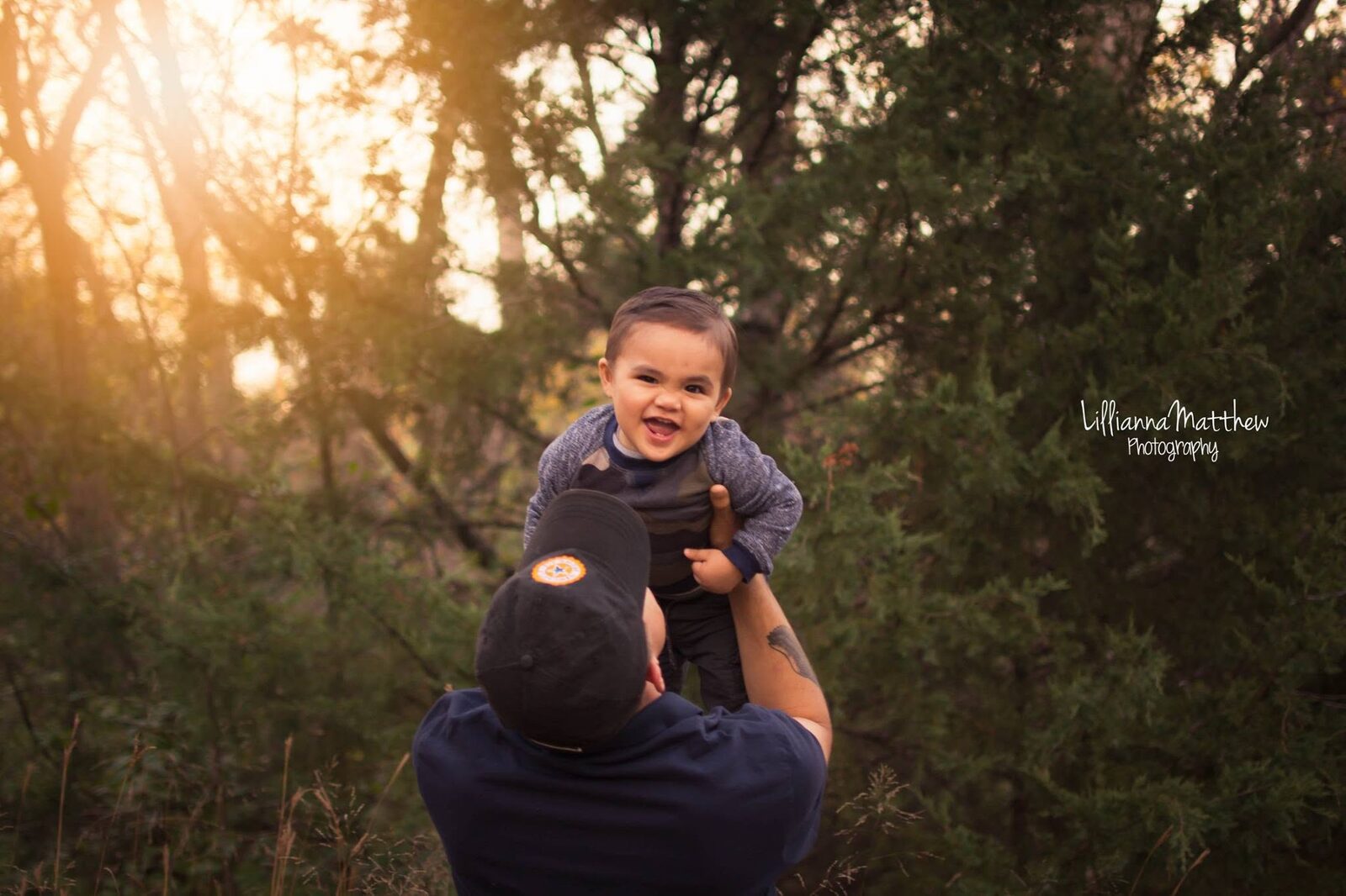 Father tossing his toddler son into the air, backlit by golden-hour forest light