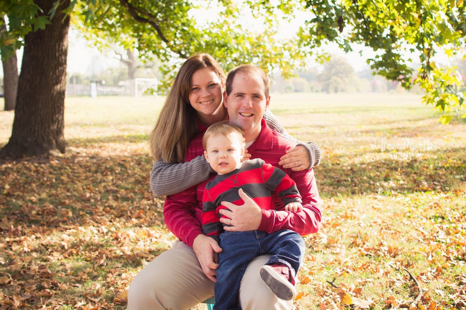 Family of three embracing in an autumn park, coordinated in red and black plaid