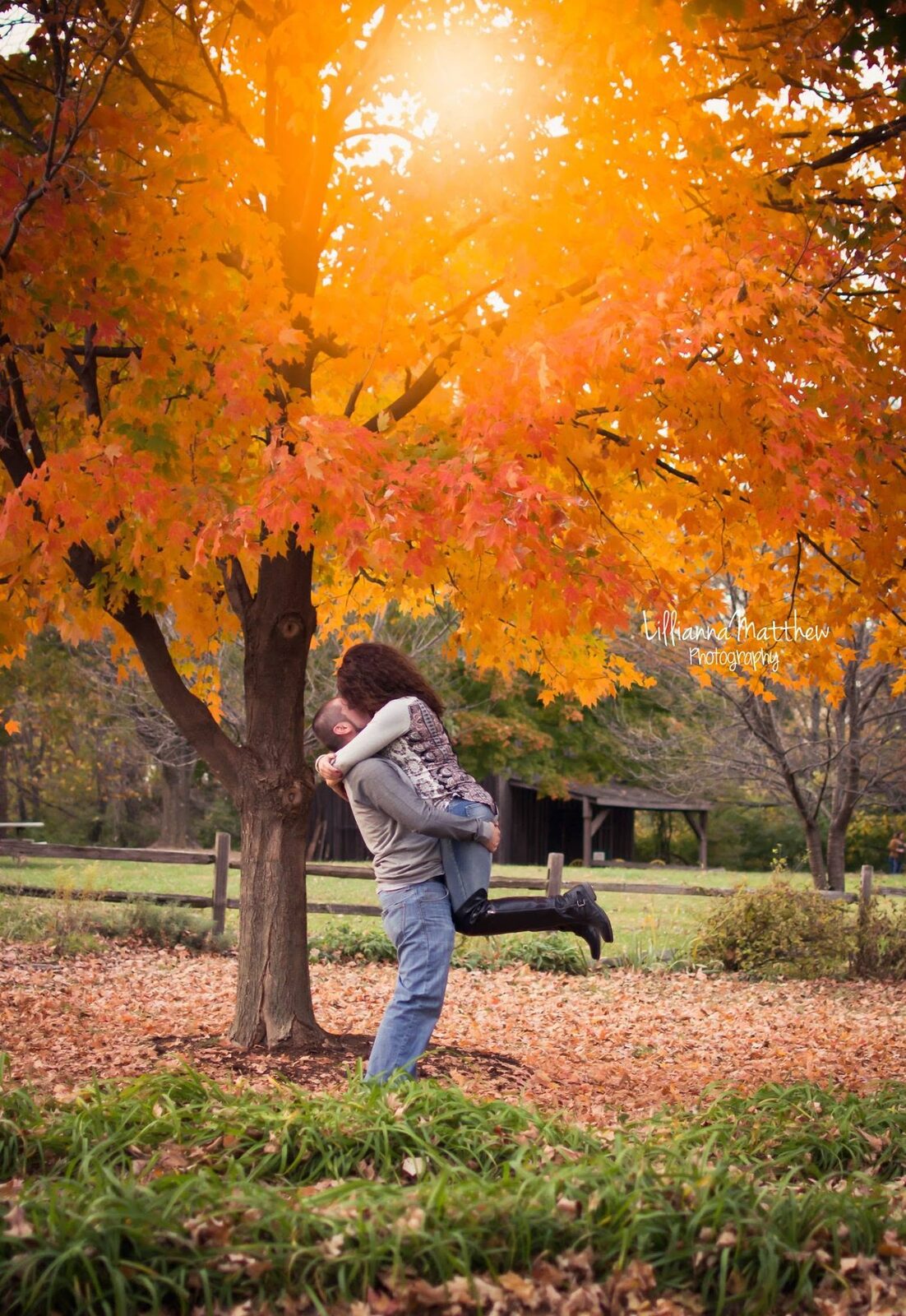 Couple kissing under a golden fall tree with the sun flaring through the leaves
