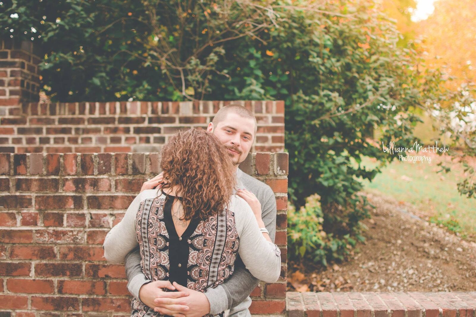 Couple embracing in front of a brick wall, man smiling over his partner's shoulder