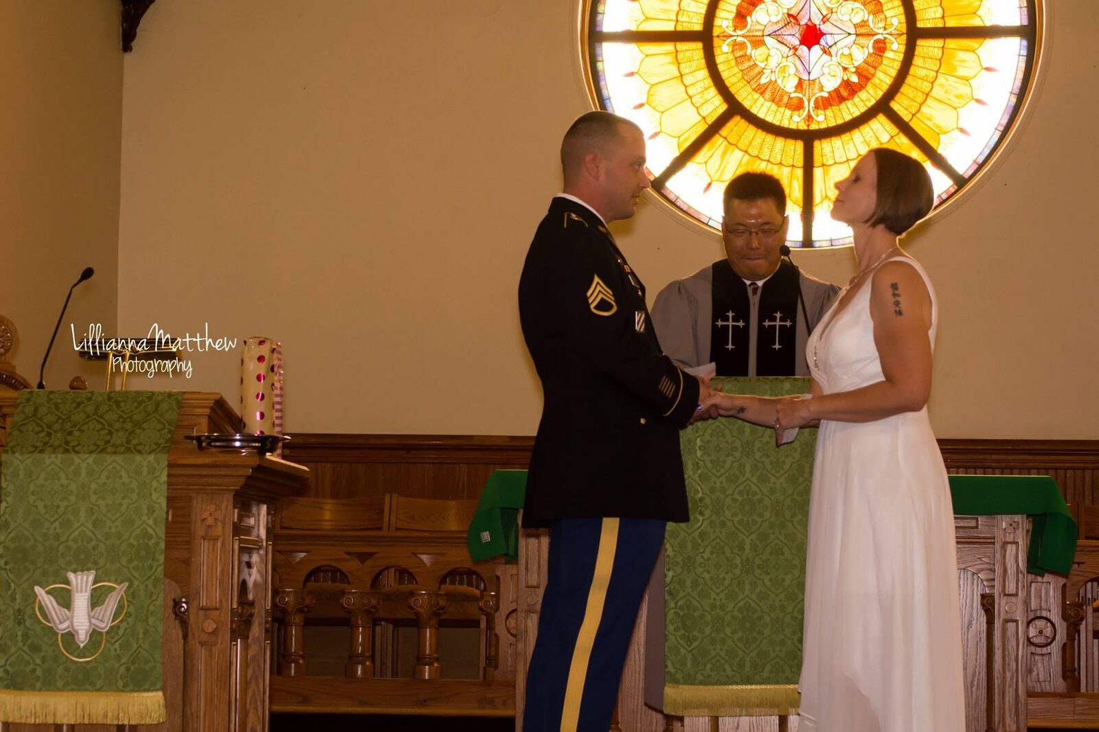 Couple in military dress holding hands at the altar in front of a stained glass window