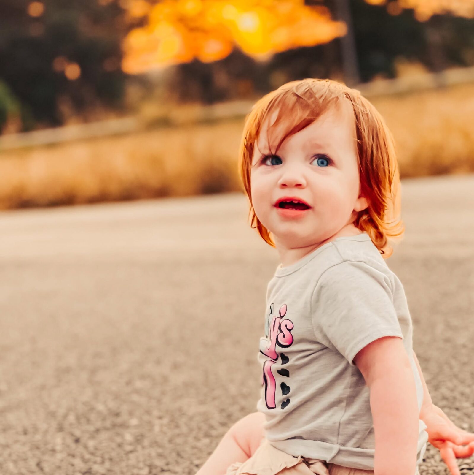 Toddler girl sitting on a road at golden hour, backlit by a warm sunset