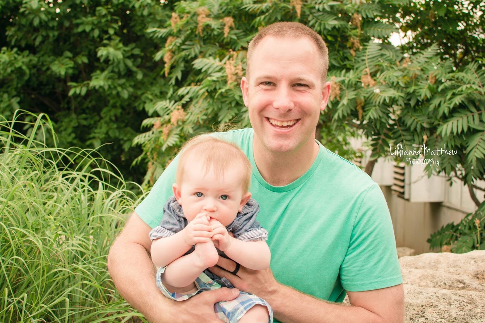 Dad laughing while holding his baby, who plays with her own feet, in a candid garden setting
