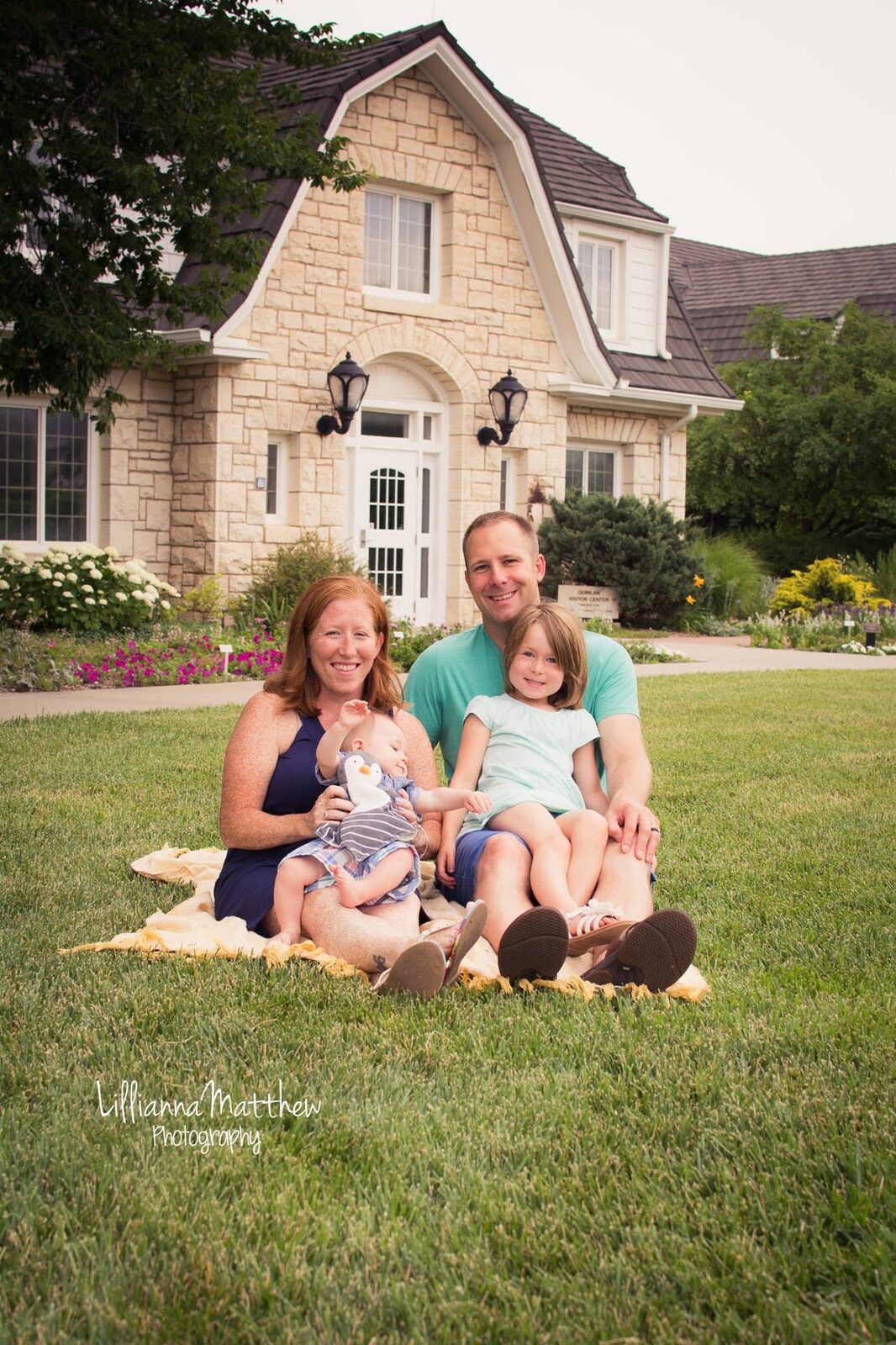 Full family of four smiling together on the lawn in front of their house