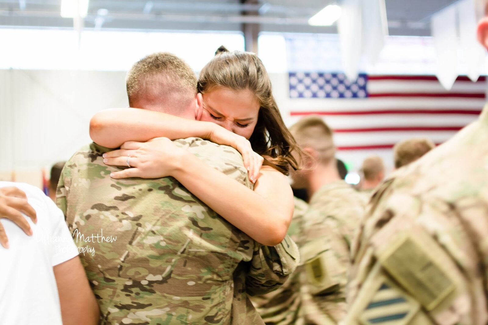 Tearful, emotional embrace between a soldier and his wife in front of an American flag