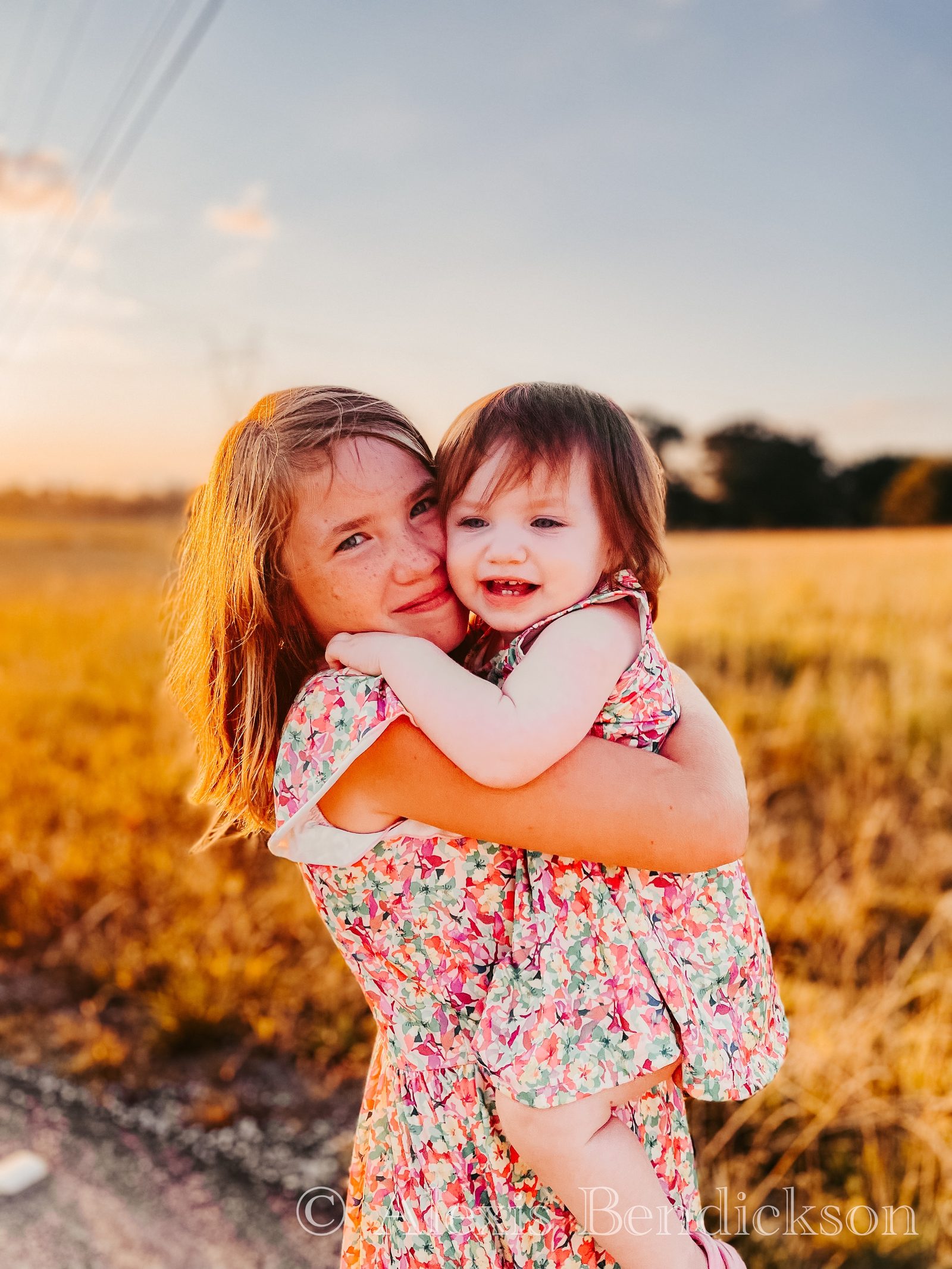 Arianna hugging Emme cheek to cheek in a field at sunset