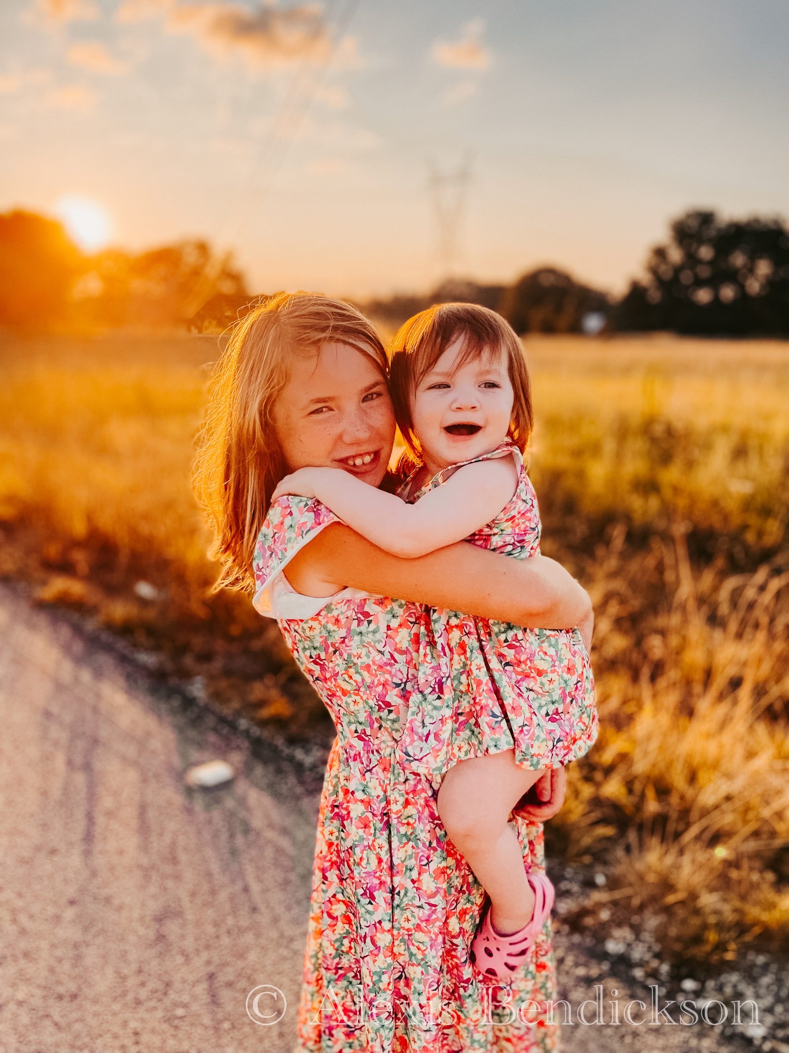 Arianna holding Emme, both grinning at the camera at sunset