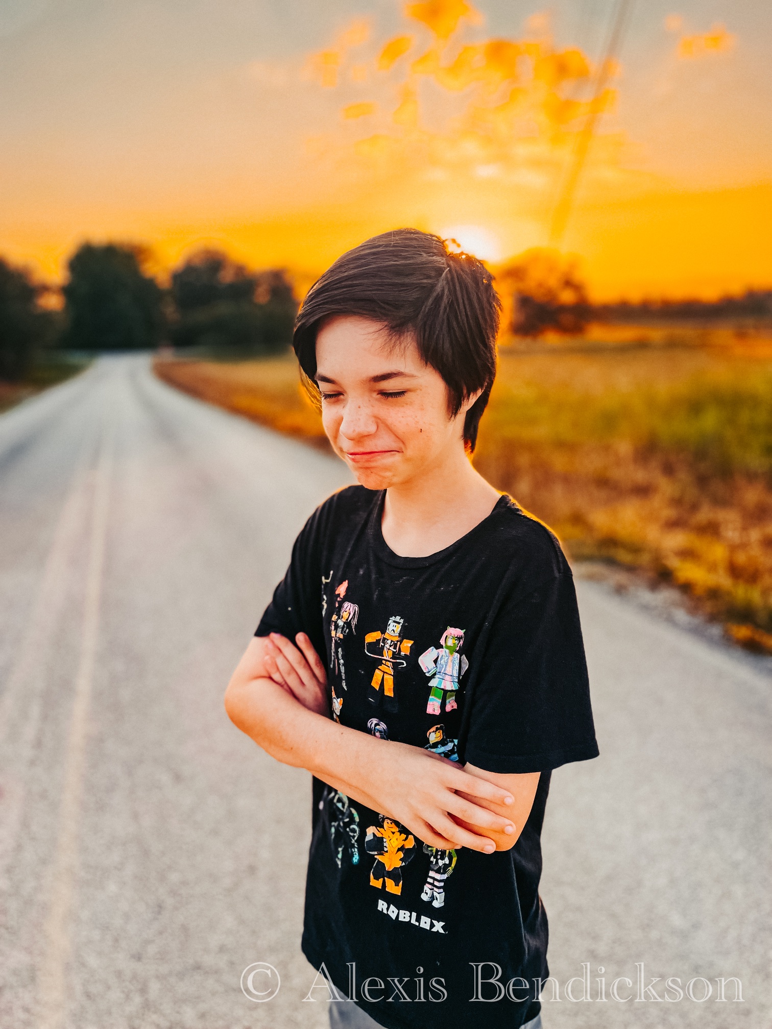 Golden hour portrait of Noah in a Roblox t-shirt with arms crossed on a country road