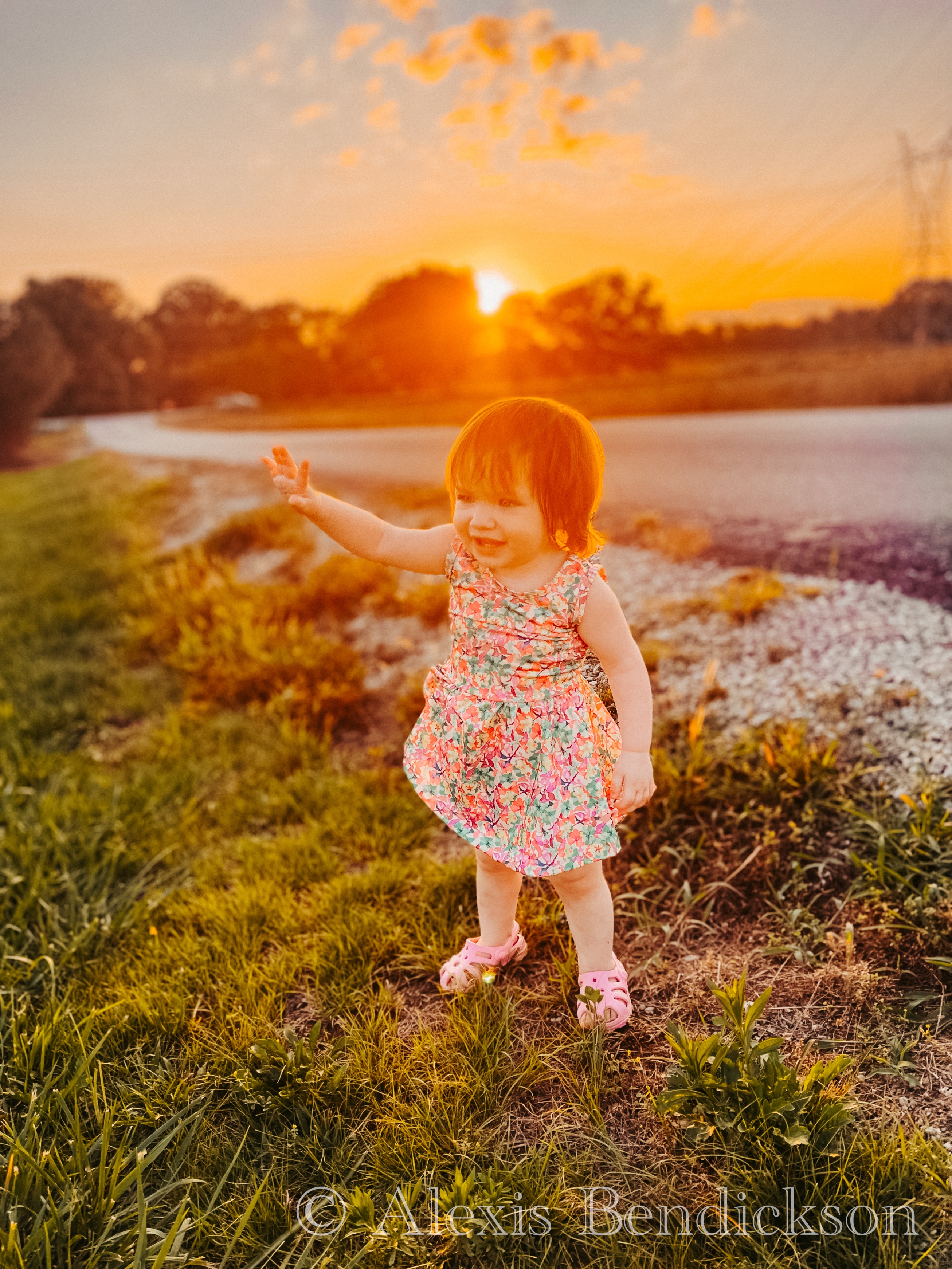 Emme in a floral dress with arm outstretched, smiling at sunset
