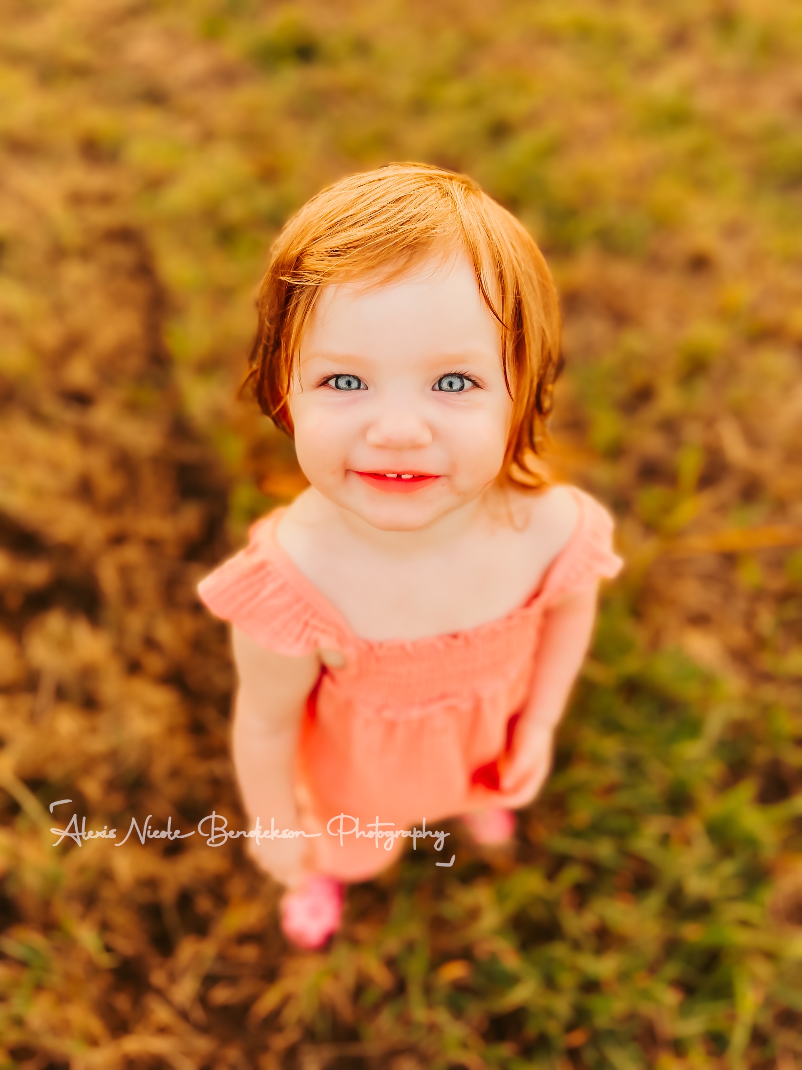 Close-up portrait of a toddler in a pink romper looking up at the camera