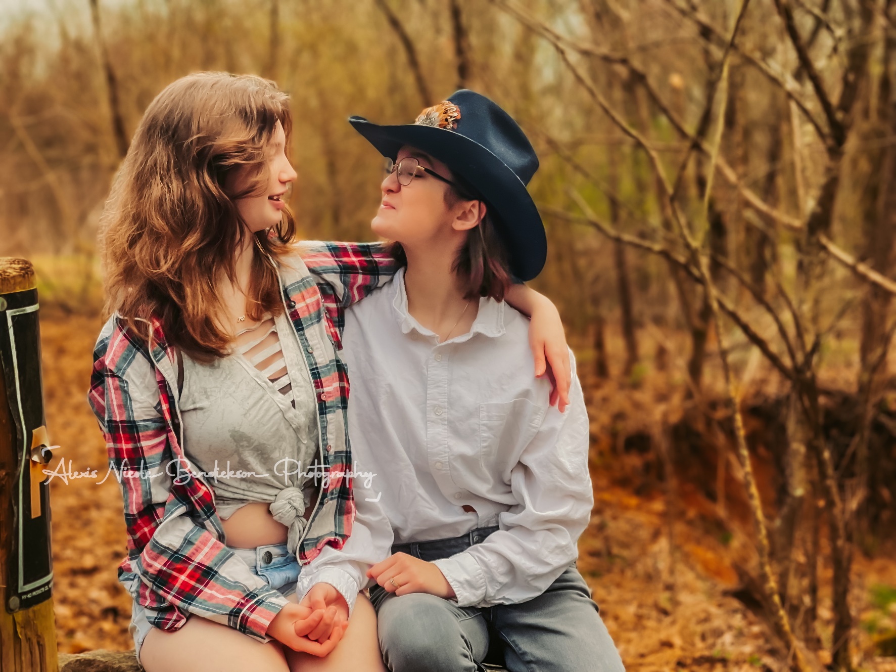 Two young people sitting together in the woods, one wearing a cowboy hat