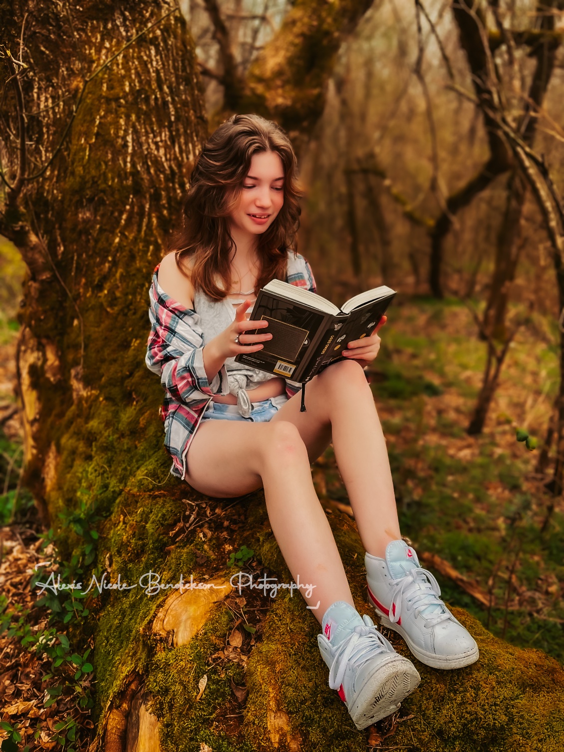 A young woman reading a book on a mossy tree trunk in the woods