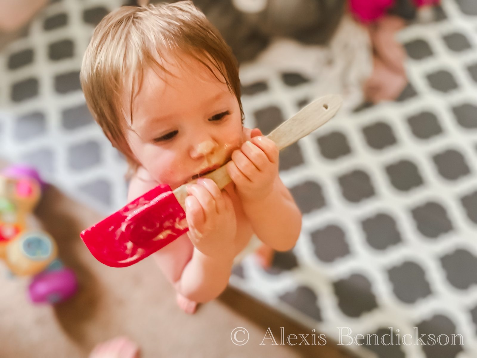 Toddler Emme biting a red spatula while baking