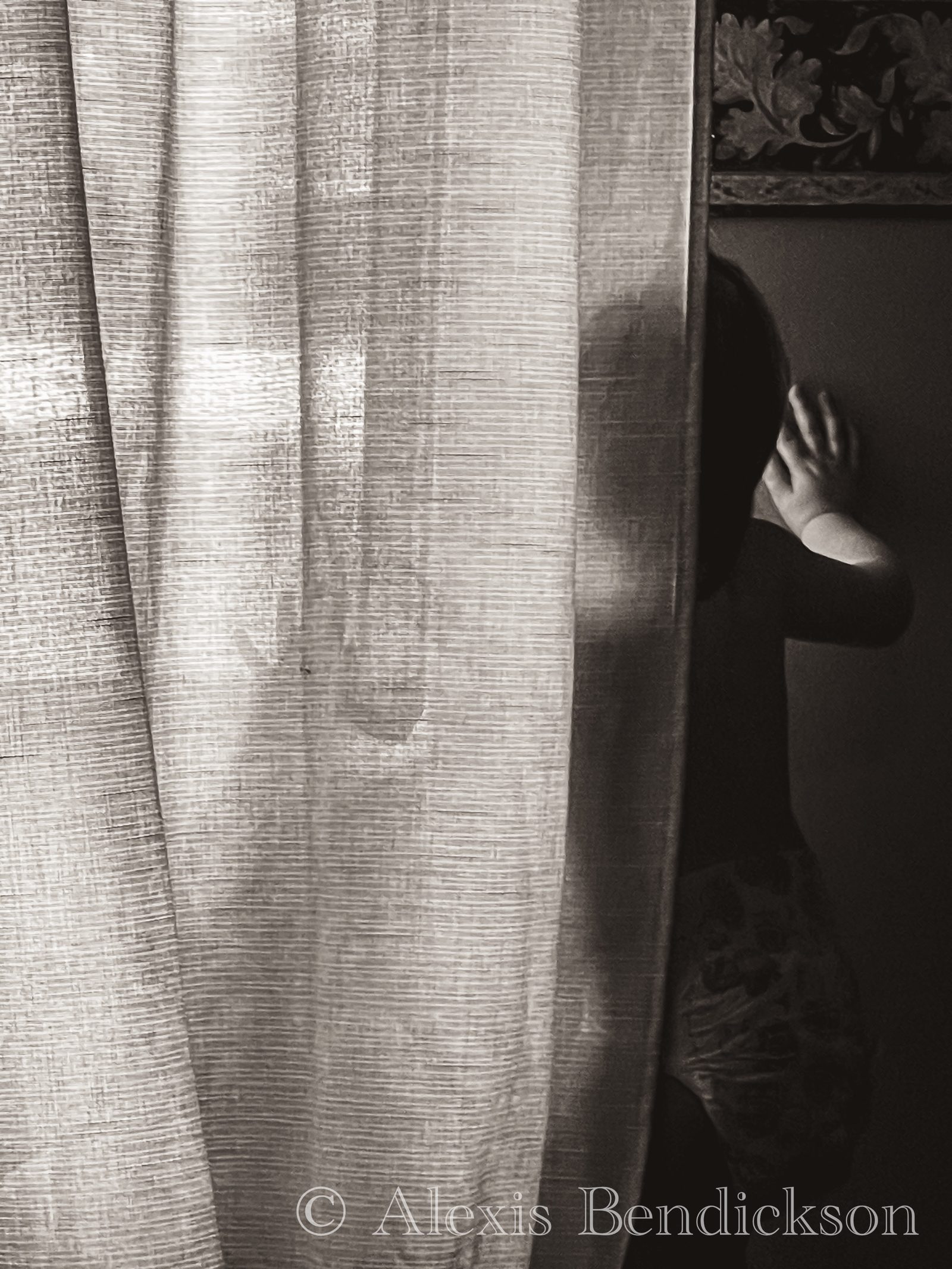 Small child peeking out from behind a sheer curtain, black and white