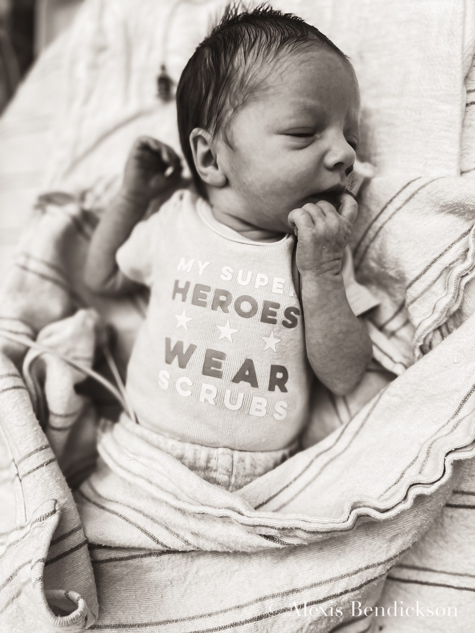 Emme sleeping in the NICU in a 'my super heroes wear scrubs' onesie, black and white, February 2022