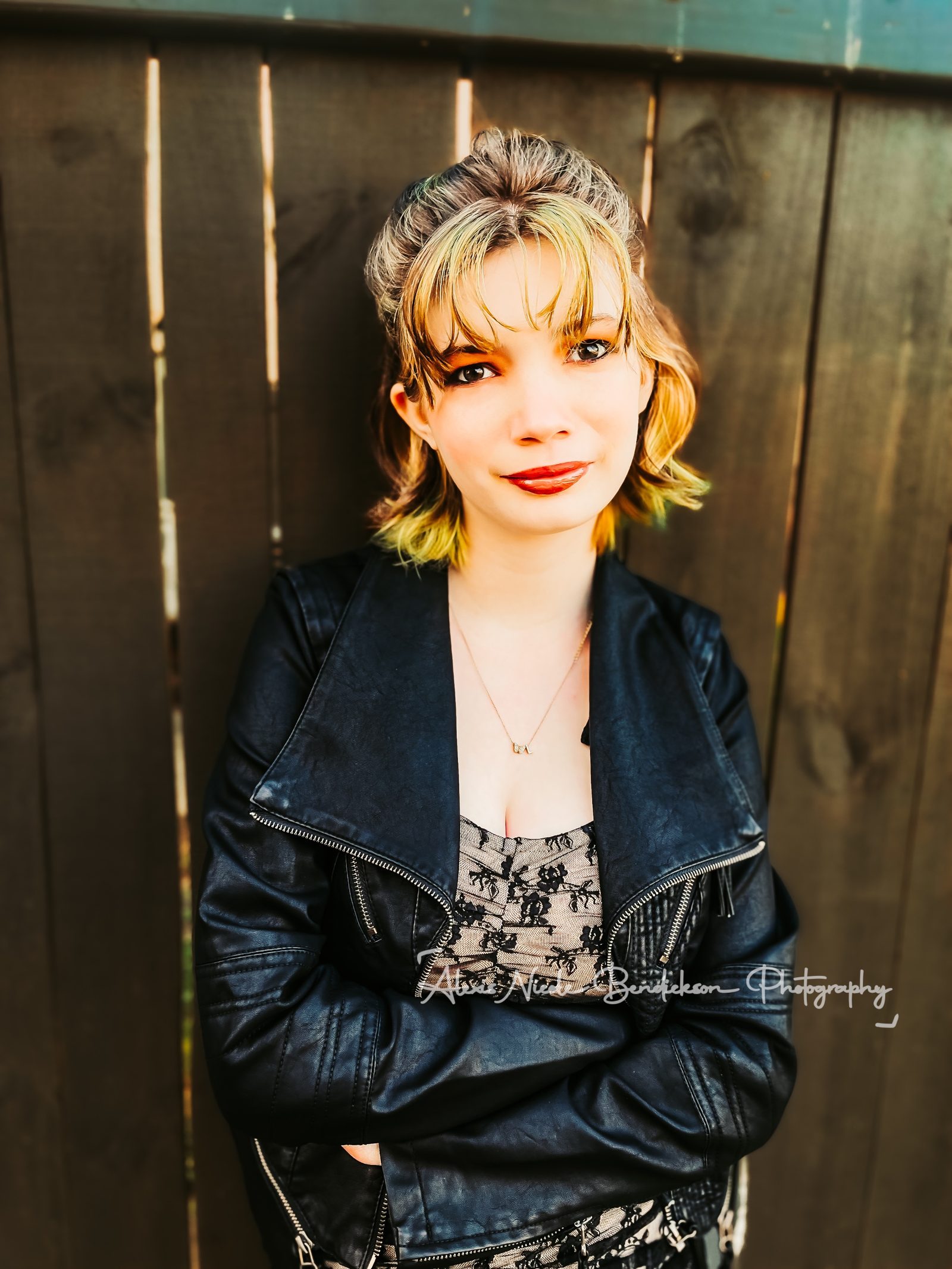 Lillia in a leather jacket against a wooden fence, color portrait