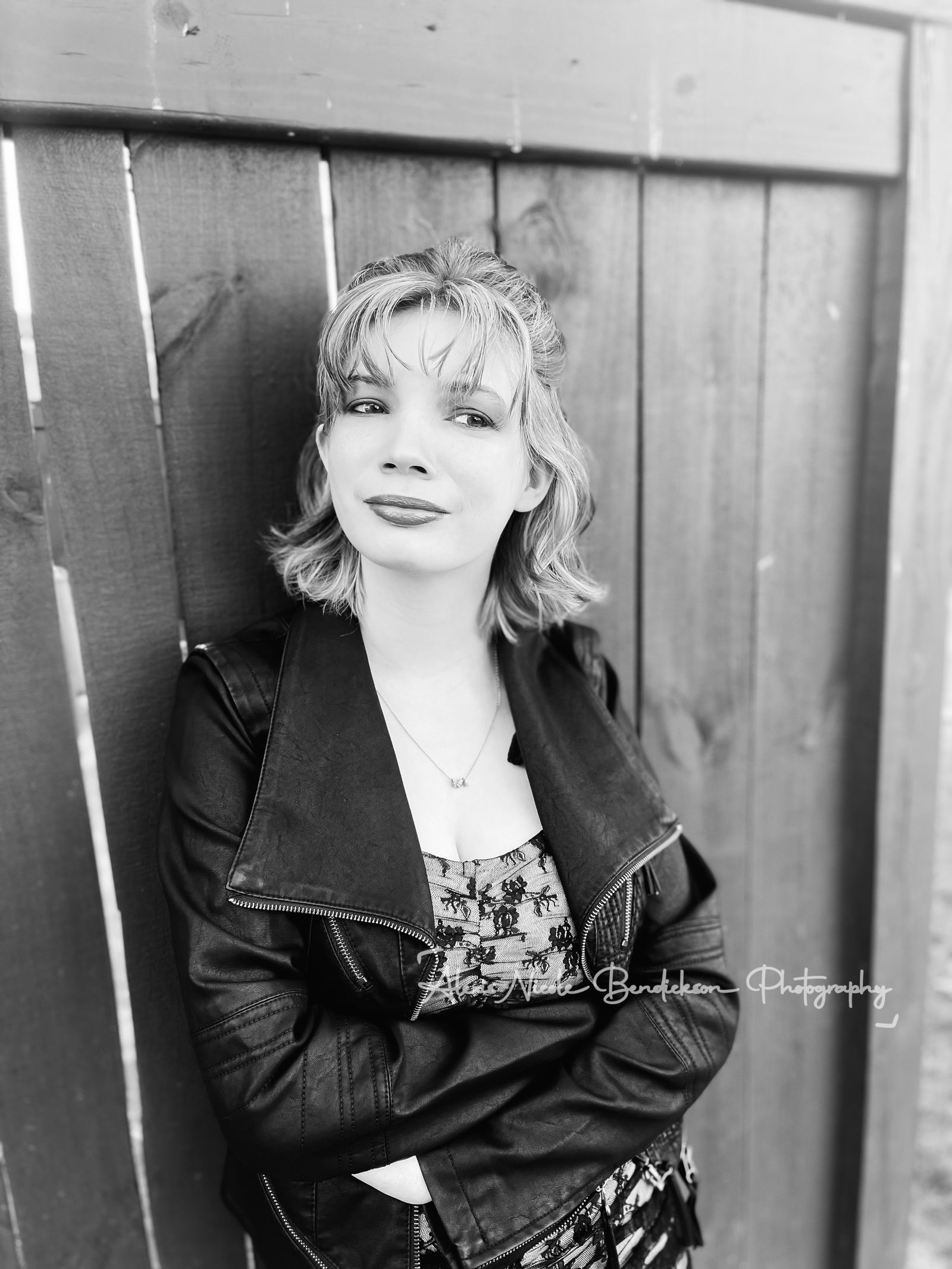 Lillia in a leather jacket against a wooden fence, black and white portrait