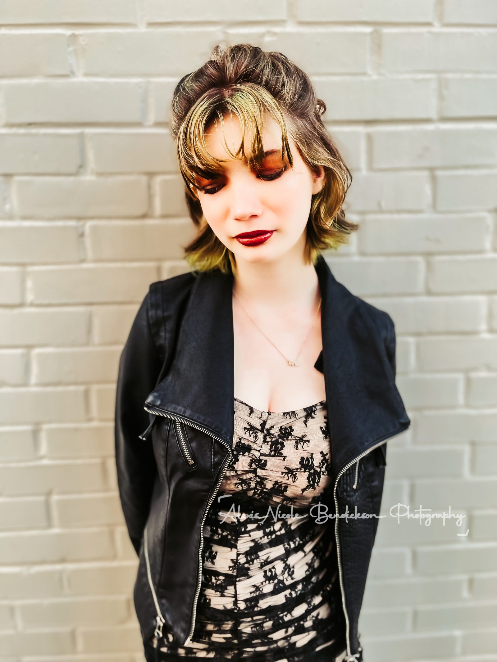 Lillia against a brick wall, eyes lowered