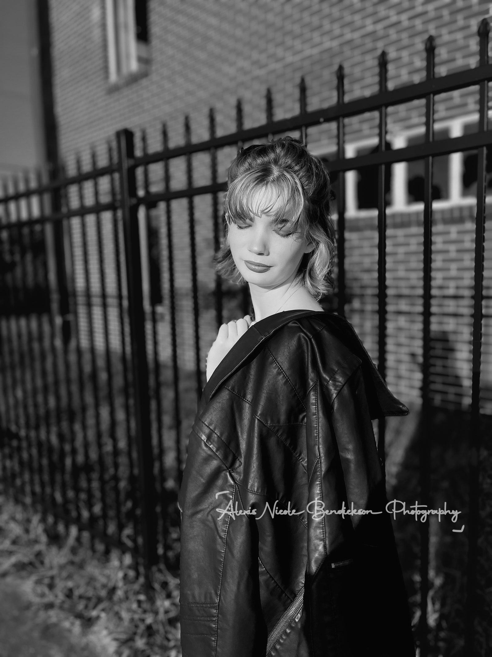 Lillia looking over her shoulder by an iron fence, black and white