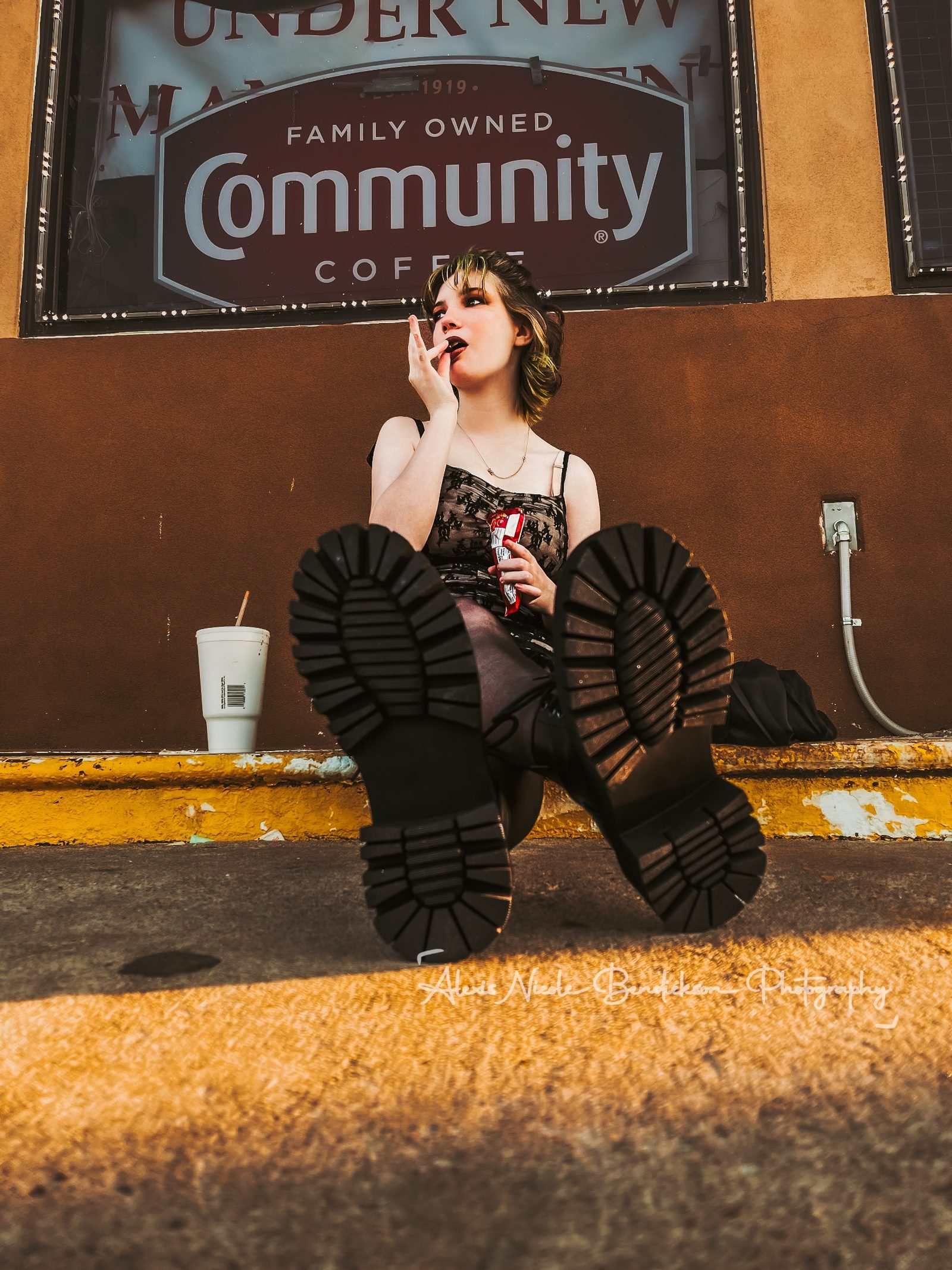 Low-angle shot of Lillia's boots, hand to her mouth, against a storefront